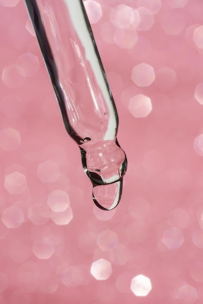 Pipette cosmétique avec une goutte sur fond rose