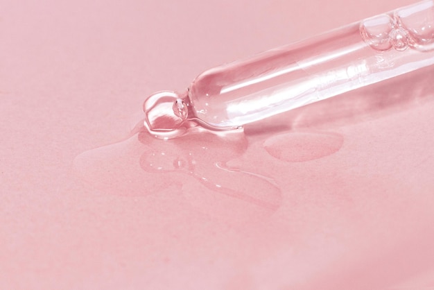 Pipette cosmétique avec liquide dégoulinant et gouttes sur fond rose sérum sérum gel vitamine eau huile