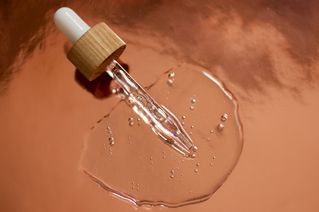 Pipette avec couvercle en bois et compte-gouttes dans le gel cosmétique. Vue de dessus, cosmétique liquide, macrophotographie. Beau fond métallique, espace de copie pour le texte.