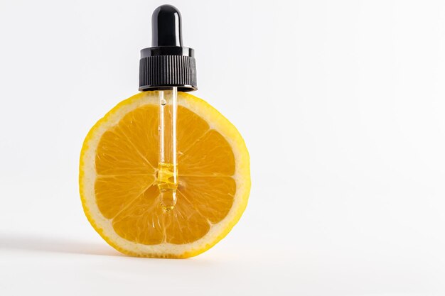 Pipette en verre cosmétique remplie de remède naturel au citron sur une tranche verticale de fruits mûrs vue de face gros plan espace pour le texte