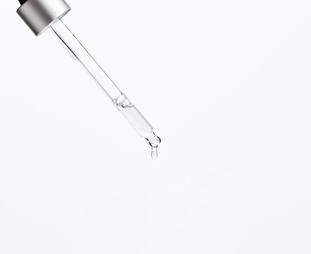 pipette en verre avec liquide transparent dégoulinant sur fond blanc. Acide, sérum