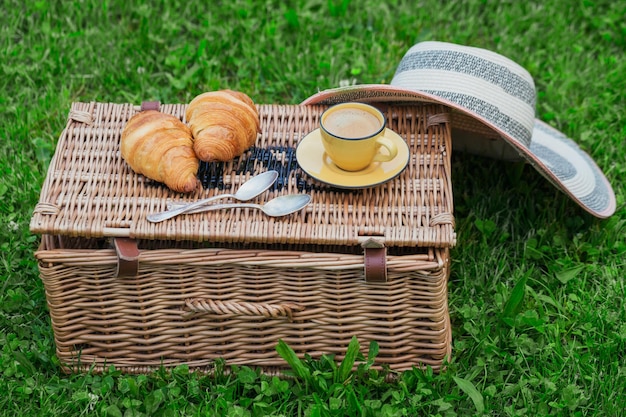 Pique-nique au parc sur l'herbe panier en osier croissants frais et café