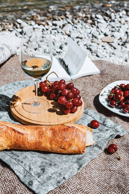 pique-nique sur la côte avec verre de vin blanc baguette cerises raisin livre ouvert oreiller