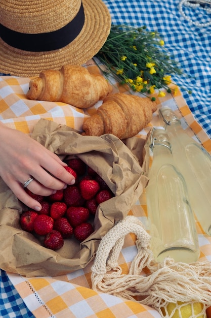 Un pique-nique avec des croissants, des fraises, de la limonade sur une couverture à carreaux.