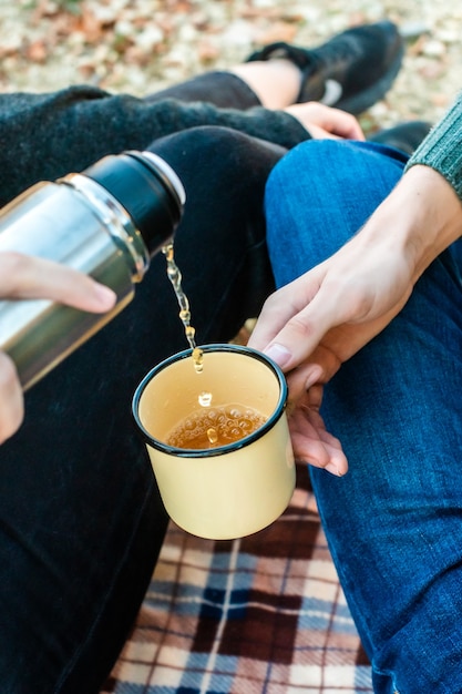 Pique-nique dans la forêt d'automne. les mains des femmes versent le thé d'un thermos dans une tasse rétro. promenade romantique automne