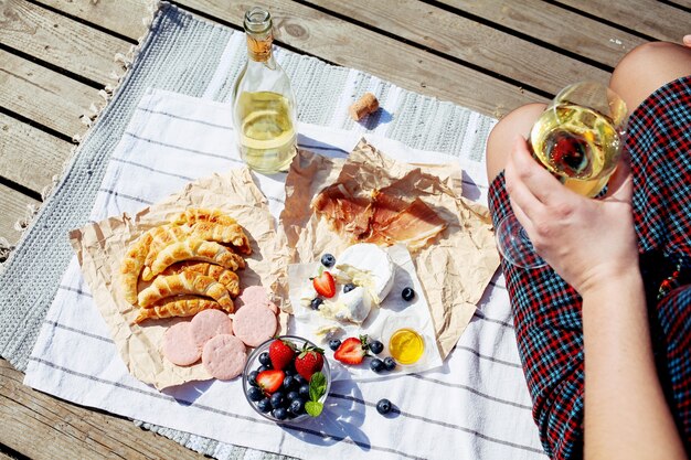 Pique-nique esthétique en plein air avec verres à vin, croissant, camembert et fruits.