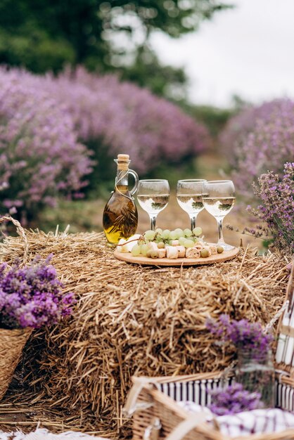 Pique-nique d'été dans le champ de lavande. Verres de vin, panier pique-nique, collations et bouquets de fleurs sur une botte de foin parmi les buissons de lavande. Mise au point sélective douce.