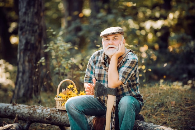 Pique-nique d'été ou de printemps. Agriculteur s'asseoir sur du bois. Vieux sage. Homme mûr avec barbe au chapeau. Humain et nature. Détendez-vous en forêt. Homme réfléchi. Homme barbu au chapeau sur fond d'arbres.