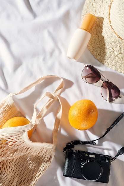 Pique-nique à plat, avec des lunettes, un sac orange, de la crème solaire et un chapeau de paille avec de l'espace. Ambiance estivale