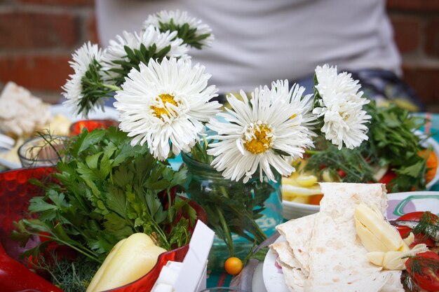 Pique-nique en plein air, assiette jetable avec collations, un verre de vodka et un bouquet d'asters blancs