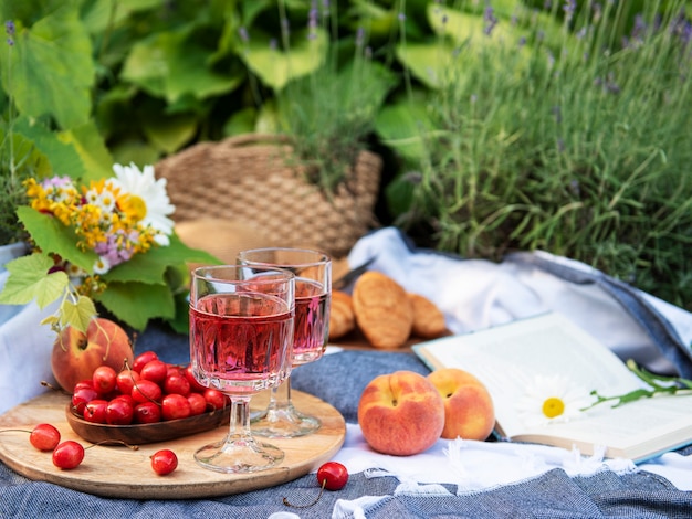 Pique-nique en plein air dans les champs de lavande. Vin rosé dans un verre, cerises et chapeau de paille sur couverture