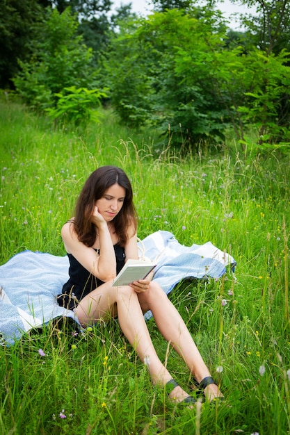 Pique-nique En Plein Air. Une Fille Lit Un Livre En Plein Air Alors Qu'elle était Assise Sur Un Plaid Bleu. La Fille Profite De L'air Frais. Loisirs De Plein Air, Gros Plan.