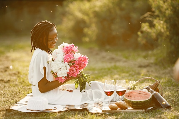 Pique-nique romantique. Belle femme afro-américaine assise seule et reniflant des fleurs. Heure d'été.