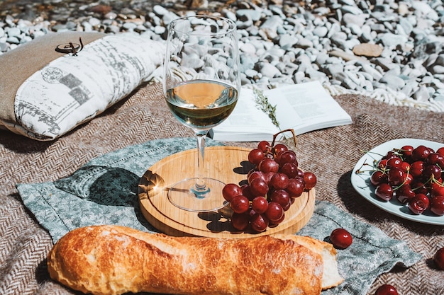 pique-nique romantique sur la côte avec verre de vin blanc baguette cerises raisin livre ouvert oreiller