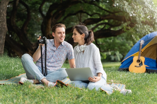 Pique-nique et temps de camping. Jeune couple s'amusant à utiliser un ordinateur portable et à camper dans le parc. Amour et tendresse, homme romantique jouant de la guitare à sa petite amie, concept de style de vie