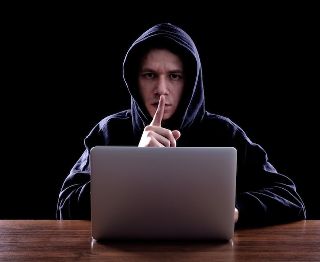 Un pirate informatique à capuche volant des informations avec un ordinateur portable Arrière-plan sombre