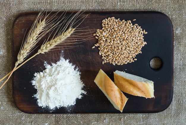 Épis de blé, céréales, farine et pain tranché sur une planche de cuisine sur fond de sac. Vue de dessus