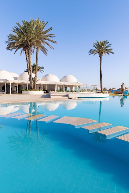 Photo piscine et palmiers avec bâtiment traditionnel avec toit en forme de dôme tunisie