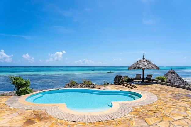 Piscine et parapluie de paille sur une plage tropicale près de la mer en journée ensoleillée sur l'île de Zanzibar Tanzanie Afrique