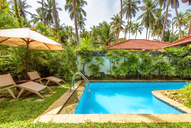 Piscine avec parasol et lits de plage dans un hôtel ou une maison tropicale Cour panoramique idyllique