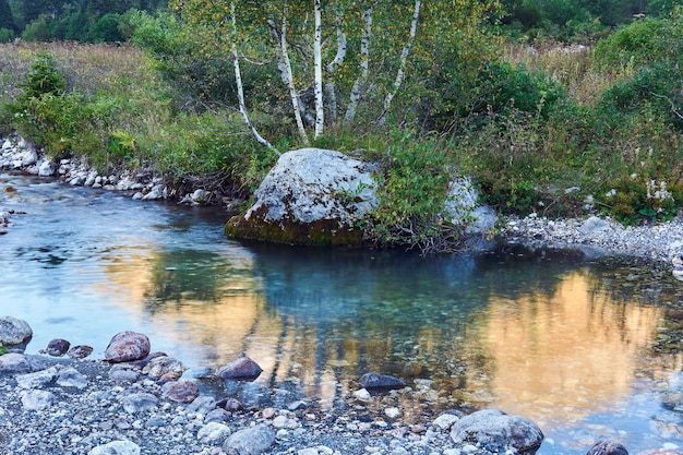 Piscine de ruisseau sur une petite rivière de montagne avec un beau rocher avec des bouleaux sur la rive