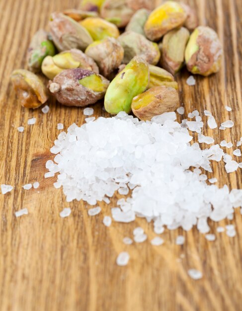 Pistaches frites vertes pelées et un tas de sel de mer blanc posé sur une vieille planche sale