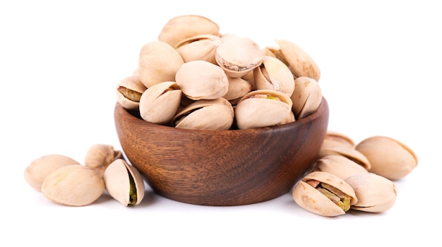 Pistaches, isolées dans un bol en bois, sur fond blanc. Pistaches grillées salées.