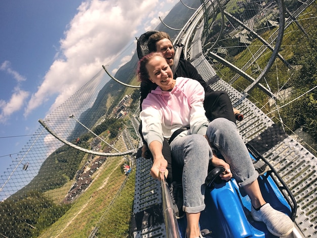 Piste de luge d'été rodelbahn avec de nombreuses courbes sur une montagne. Montagnes russes alpines en été et en automne de beaux paysages. Plaisir rapide du jeune couple voyageant.