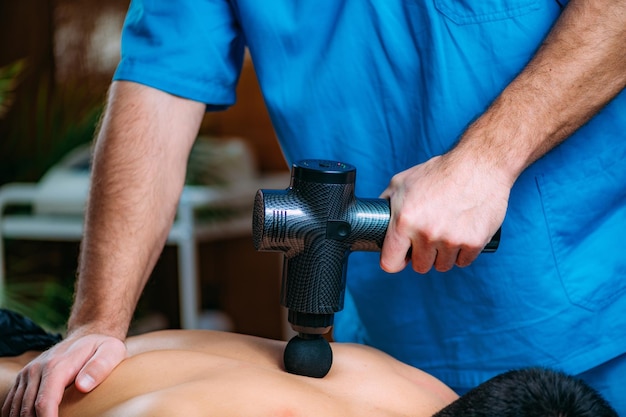 Pistolet de massage Traitement de physiothérapie Kinésithérapeute massant le dos de l'homme