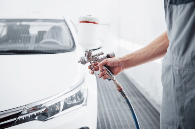 Pistolet avec de la peinture entre les mains d'un homme pour peindre une voiture.