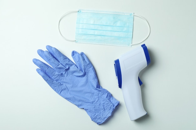 Pistolet thermomètre, masque médical et gants sur blanc