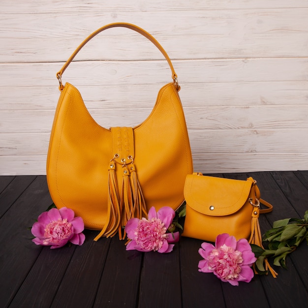 Photo pivoines corail et sac en cuir jaune sur table en bois noir.