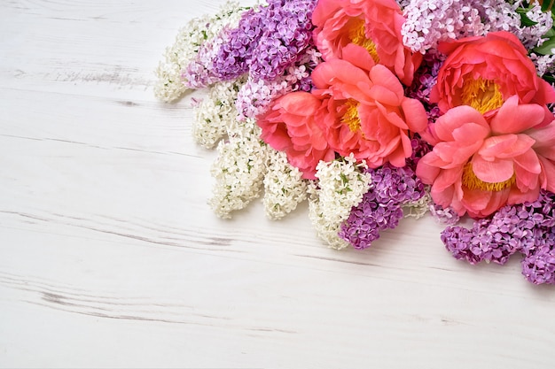 Pivoines et fleurs lilas sur fond en bois blanc.