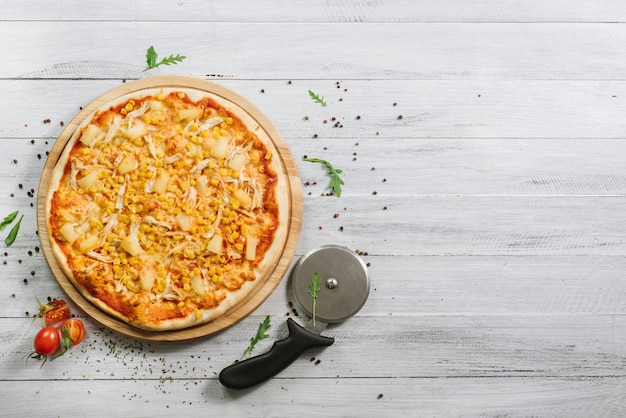 Pizza Americana avec mozzarella, filet de poulet, ananas et maïs sur fond bois