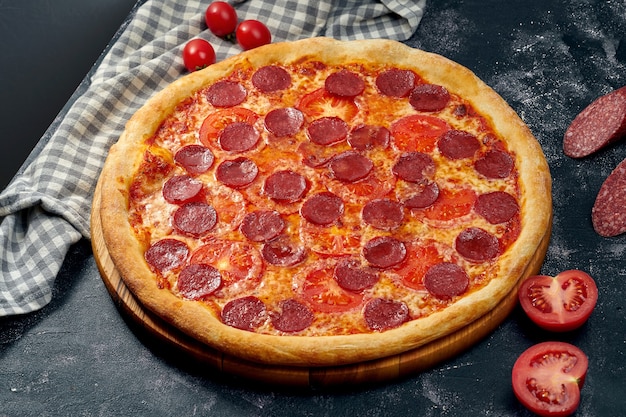 Pizza appétissante avec sauce rouge, tomates, salami et fromage. Fond sombre. Cuisine italienne