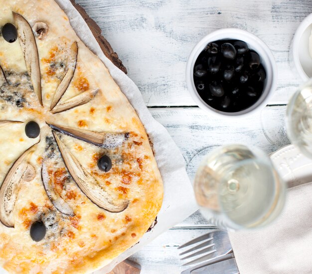 Pizza au brie et aubergine sur un fond en bois blanc.