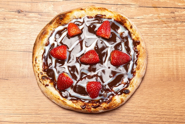 pizza au chocolat avec sauce aux fraises et à la crème sure servie sur une vue de dessus de table en bois.