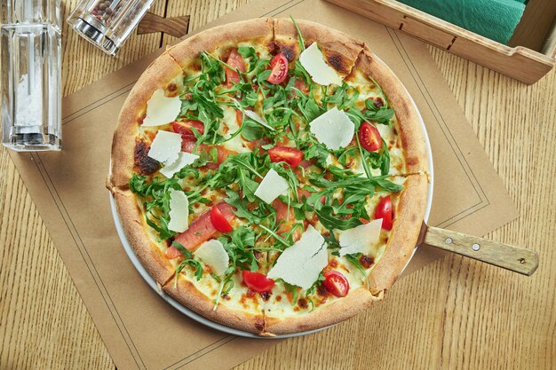 Pizza au four appétissante avec saumon, tomates cerises, parmesan et roquette avec croûte croustillante sur une table en bois. Réglage de la table du restaurant. Vue de dessus