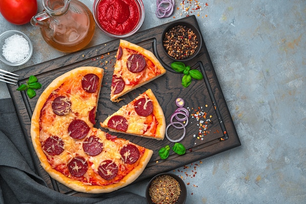 Pizza au pepperoni et ingrédients sur une planche à découper sur fond gris. Le concept d'arrière-plans culinaires. Vue de dessus, avec espace pour copier.