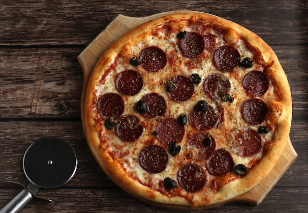 Pizza au pepperoni avec saucisses et olives sur fond de bois foncé