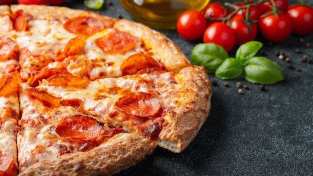 Pizza au pepperoni savoureuse et ingrédients de cuisine tomates basilic sur fond de béton noir