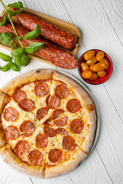 Une pizza au pepperoni et tomates sur une table en bois
