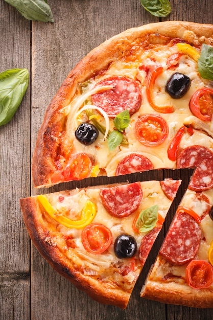 Pizza au salami et légumes sur un vieux fond en bois.