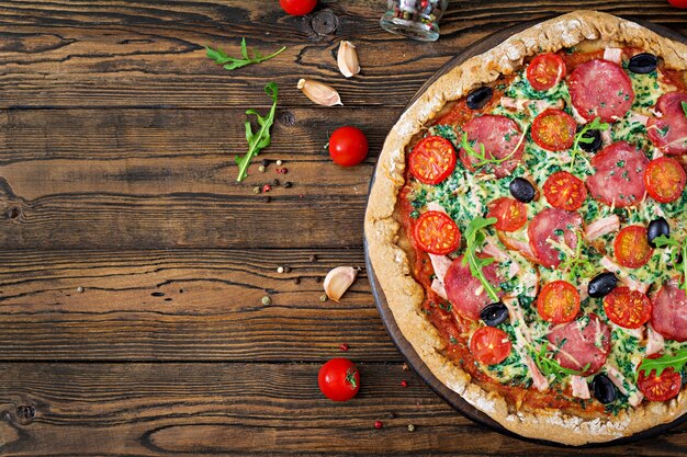 Pizza au salami, tomates, olives et fromage sur une pâte avec de la farine de blé entier. Nourriture italienne. Vue de dessus. Mise à plat.