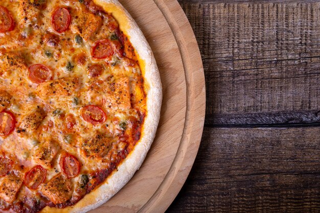 Pizza au saumon, tomates et câpres sur une planche de bois