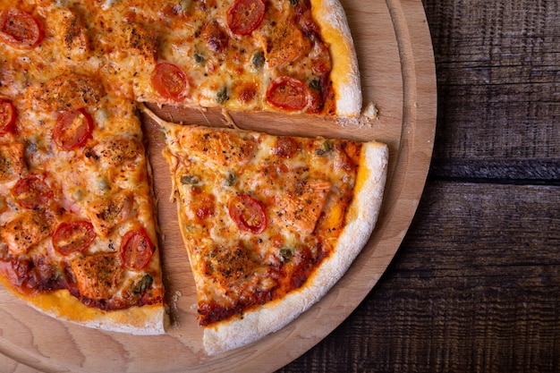 Pizza au saumon, tomates et câpres sur une planche de bois