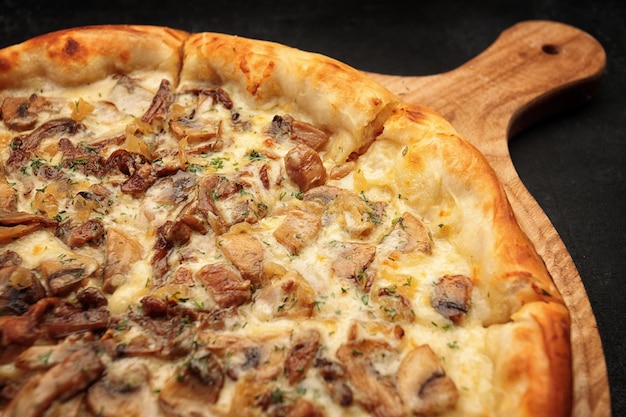 Pizza aux champignons et fromage sur une planche de bois sur fond sombre