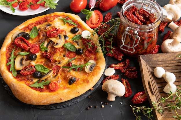 Pizza aux légumes et tomates séchées sur fond sombre dans la cuisine.