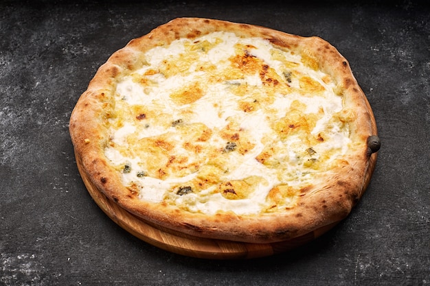 Pizza aux quatre fromages sur une planche de bois clair, sur un fond de béton foncé