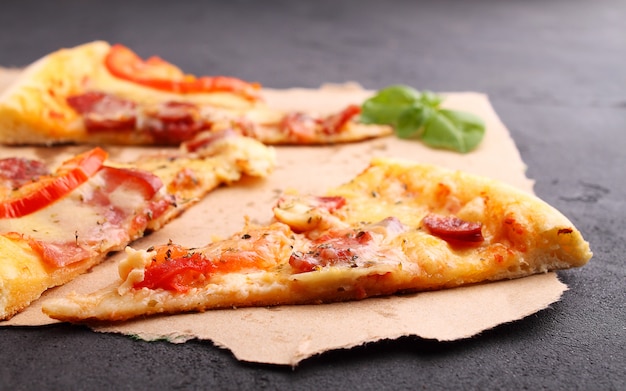 Pizza aux saucisses, jambon, tomates et fromage, décorée au basilic et coupée en morceaux sur un parchemin